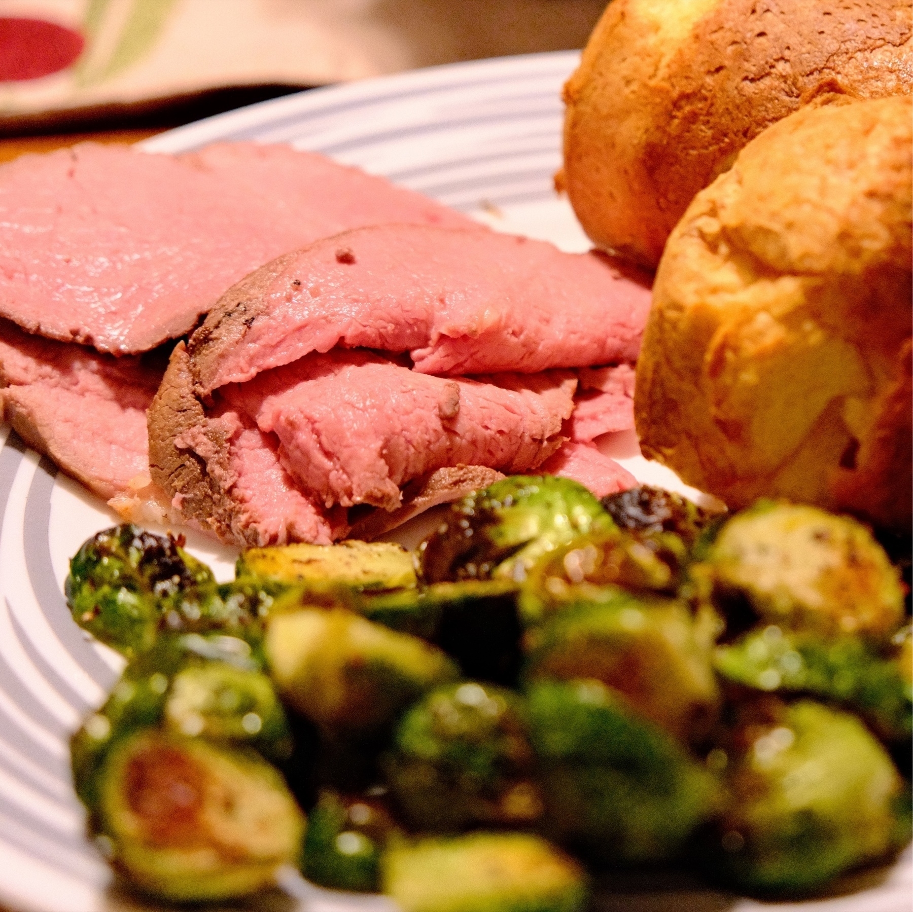 medium rare sliced roast beef with caramelized brussels sprouts and golden brown, crispy popovers