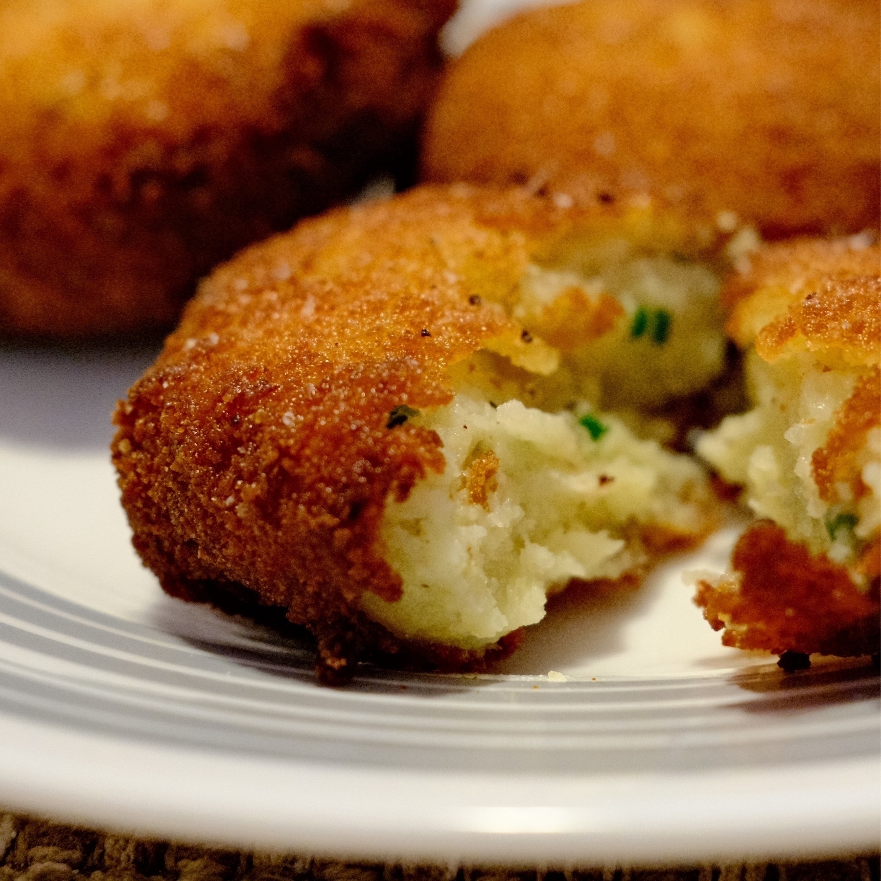 plated golden brown croquettes with one cut open, revealing fluffy white potatoes and chives