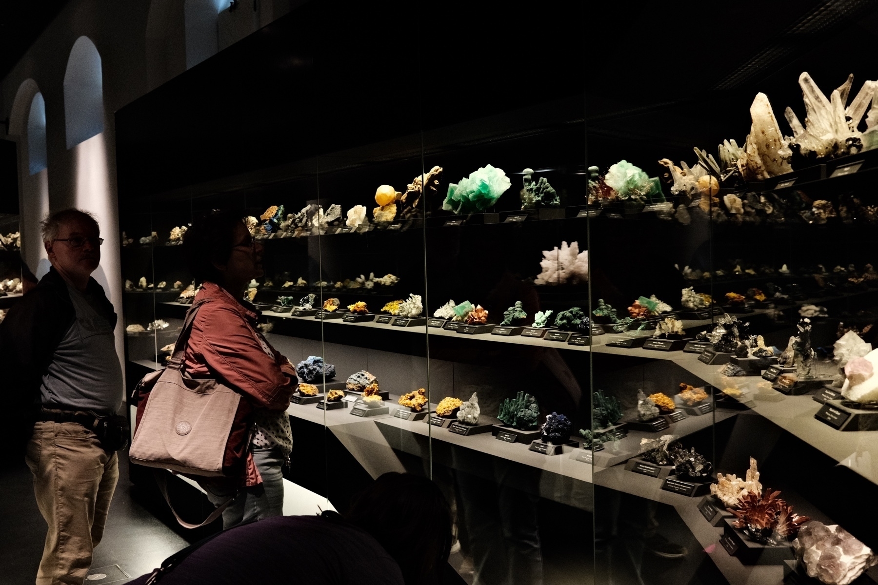 lit mineral specimens in a dark hall with two people enjoying the sights