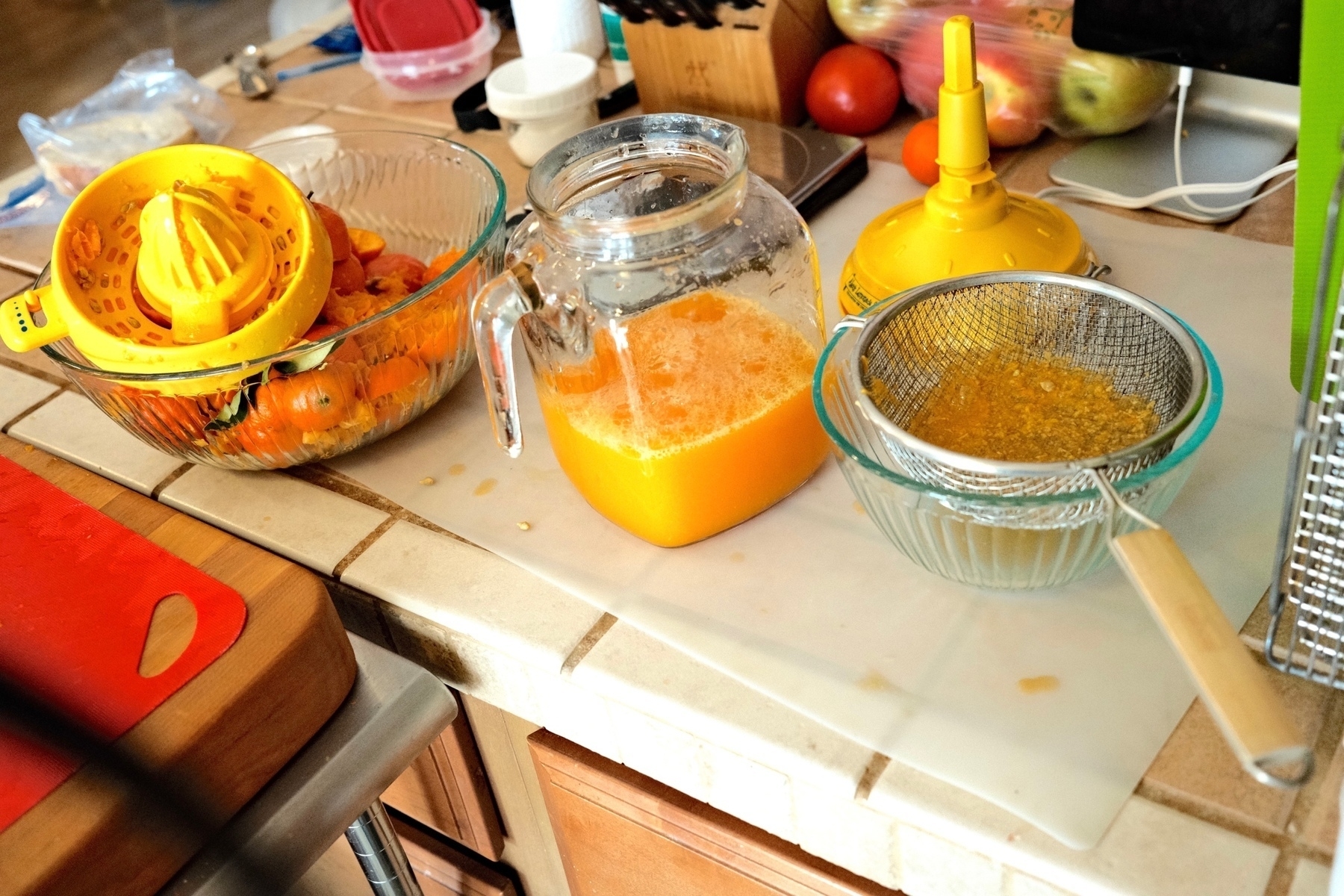 A counter covered in juicing equipment including a bowl full of rinds, a strainer sitting in a bowl, and very yellow juicer by Proctor Silex branded with Alex's Lemonade Stand.