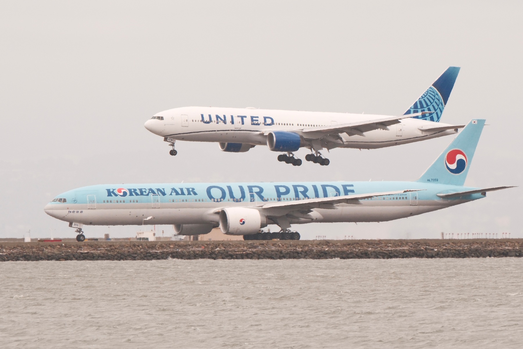 A Korean Airlines with Our Pride livery prepares for takeoff as another United 777 lands on an adjacent runway.