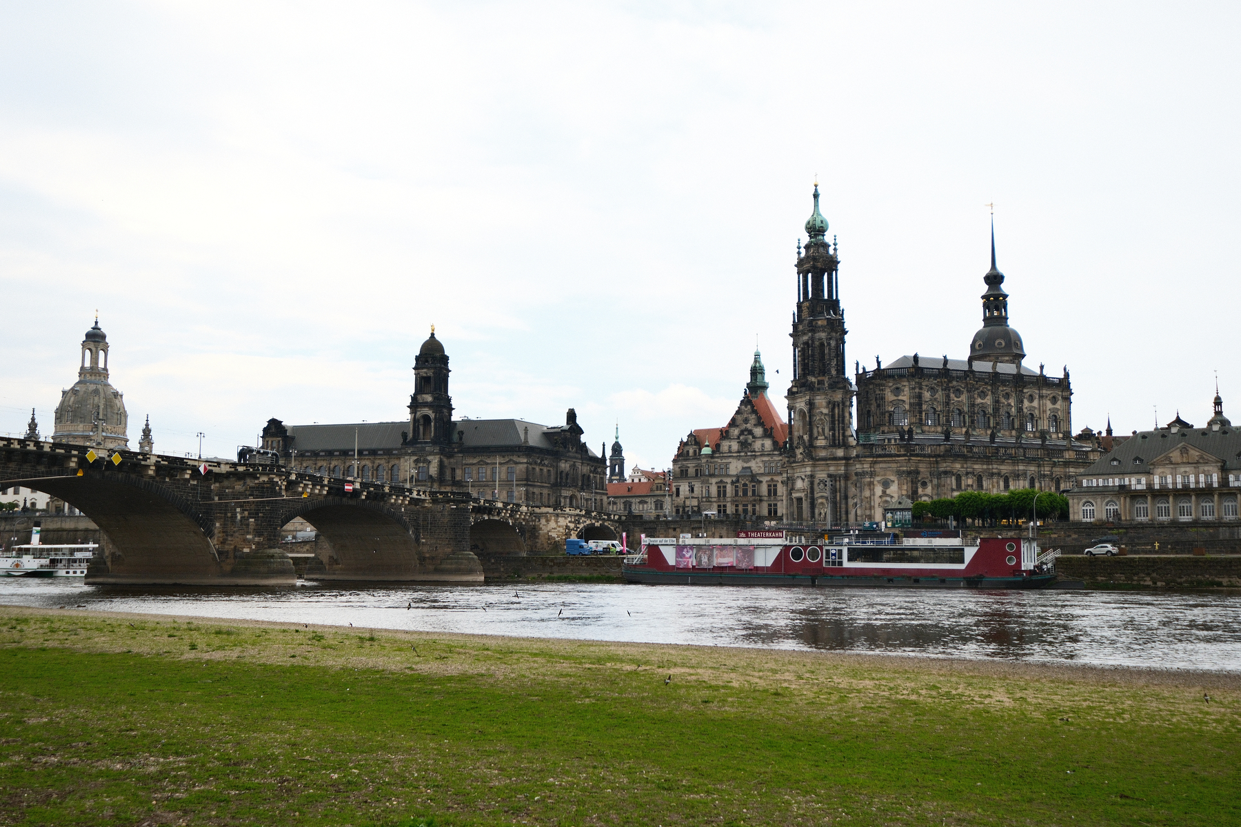 Auto-generated description: A scenic view captures a historic cityscape with a prominent bridge spanning a river, showcasing classic architecture and a riverboat in the foreground...